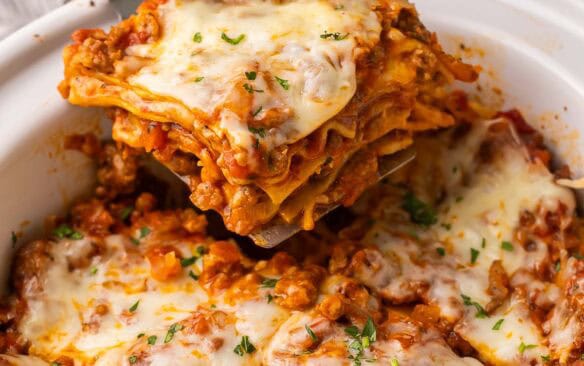 scooping a piece of lasagna out of white crockpot.