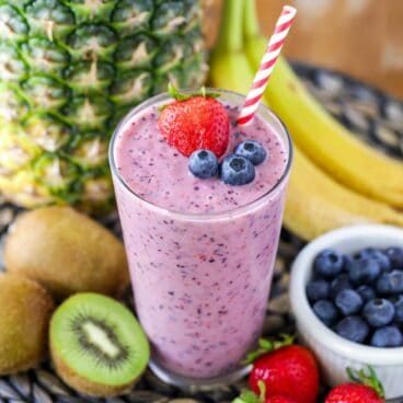 fruit smoothie in a glass with a straw and berries on top and fruit in the background.