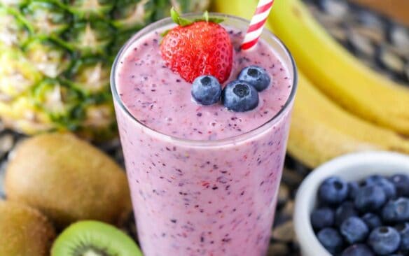 fruit smoothie in a glass with a straw and berries on top and fruit in the background.