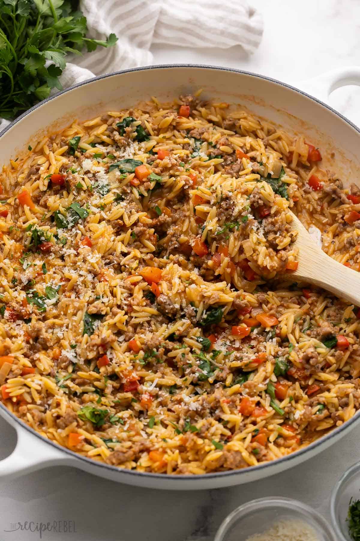 large skillet with a ladle scooping italian sausage orzo out of it.