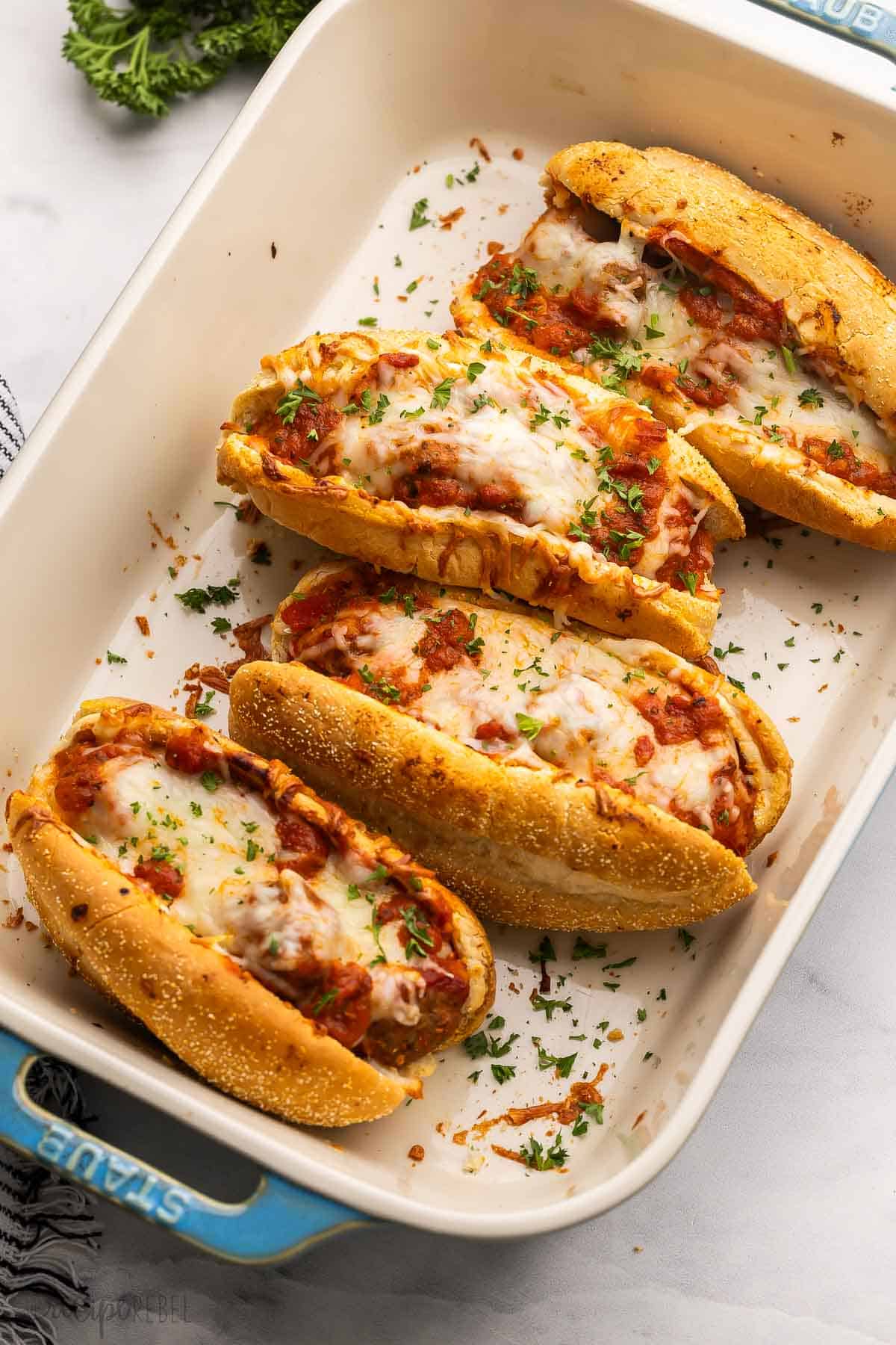 baking dish with four meatball subs topped with chopped parsley.