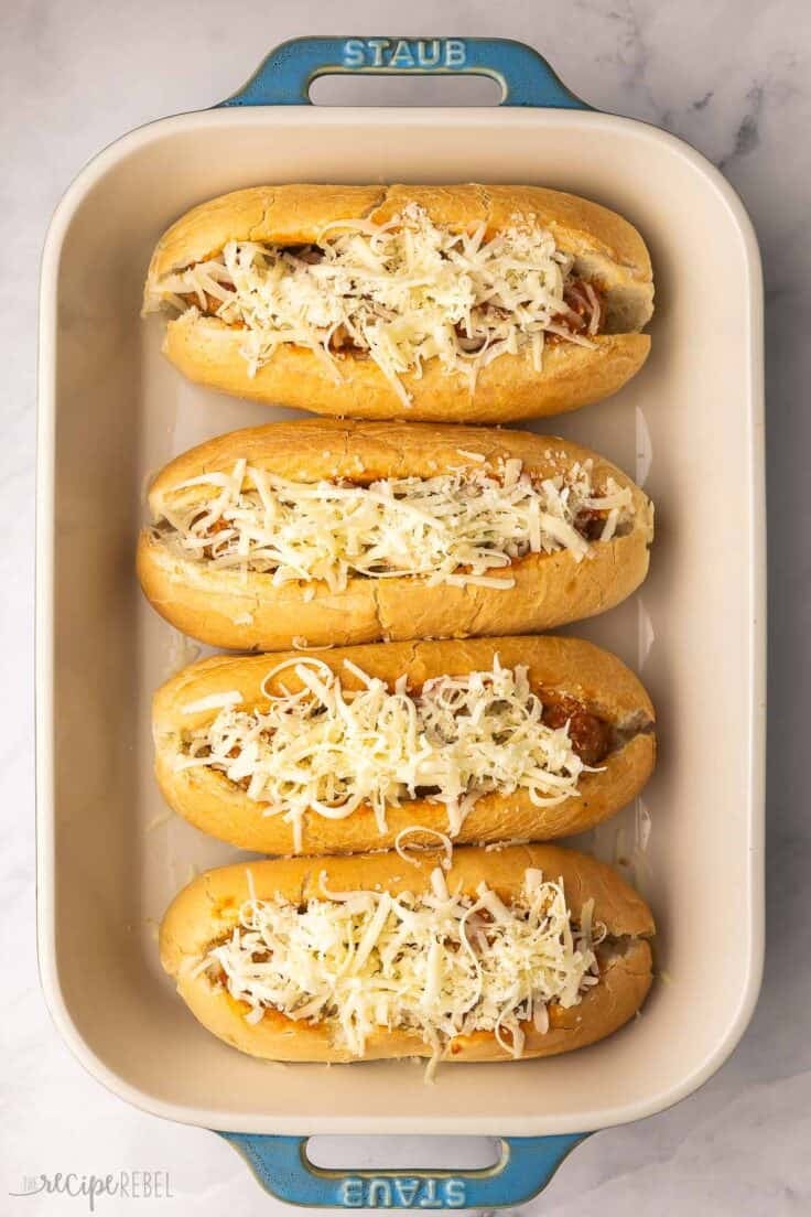 four meatball subs in pan with shredded cheese added on top.