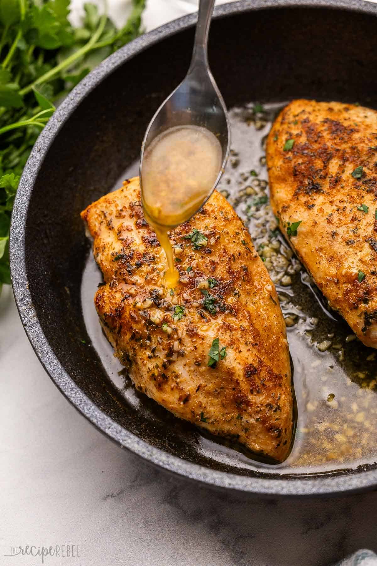 a spoon pouring buttery sauce over chicken breast.