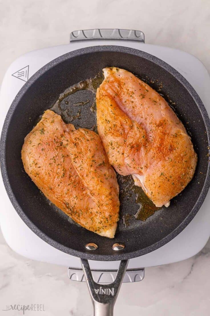 two seasoned chicken breast in black pan.