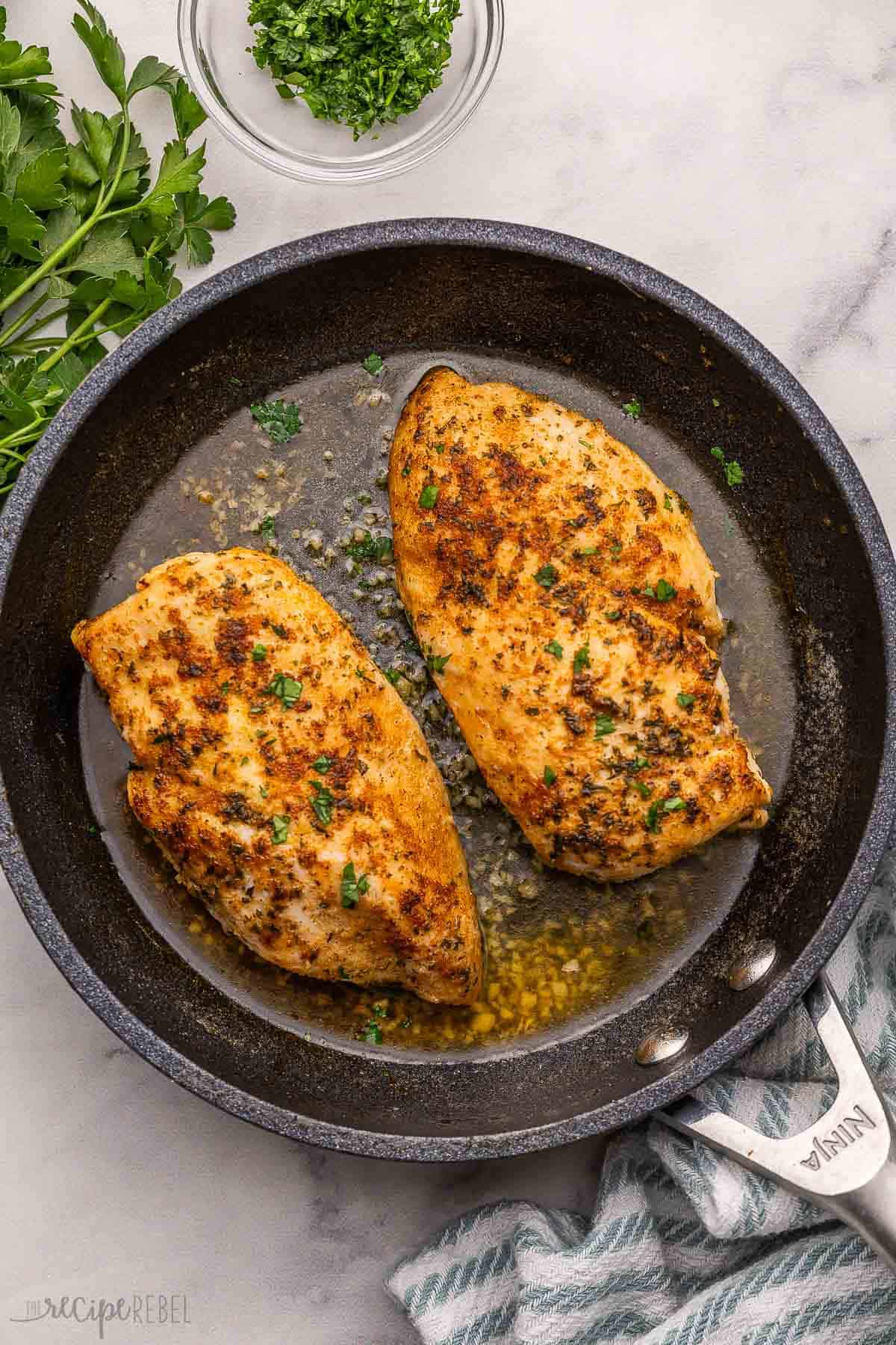 two chicken breasts in black pan with parsley beside.