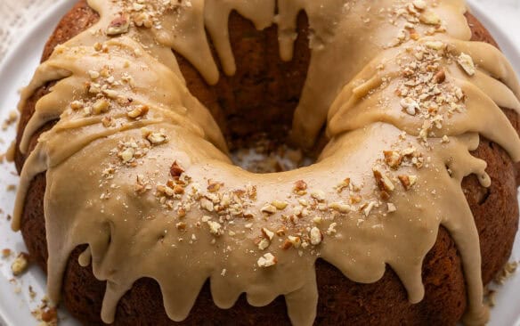 a full apple bundt cake on a white plate topped with chopped pecans.