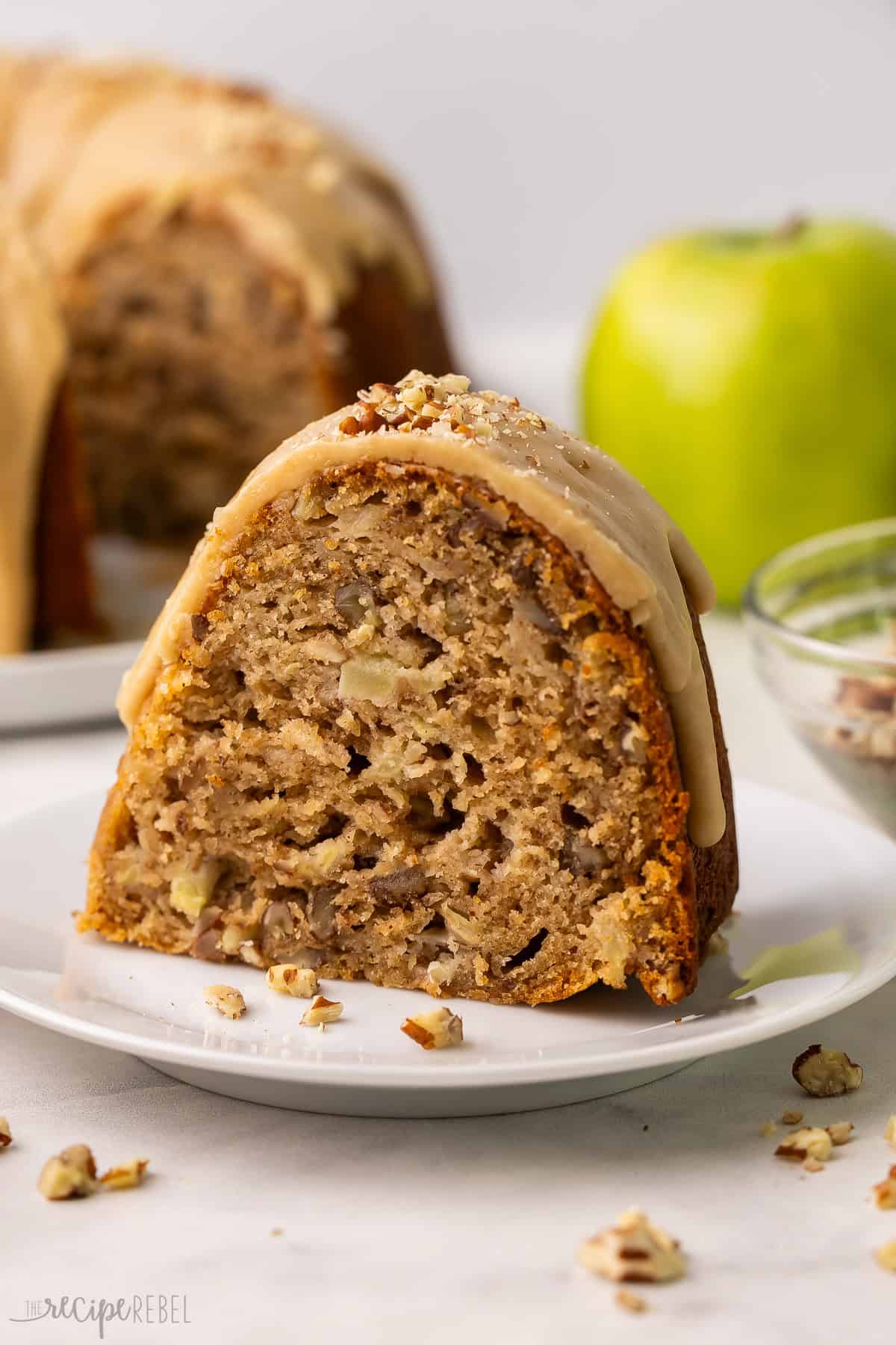 a slice of apple bundt cake on a plate with a green apple behind it.