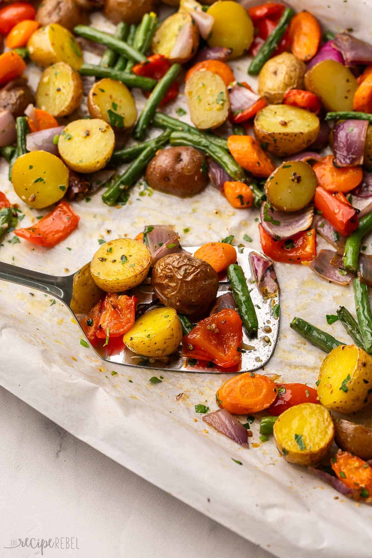 scooping roasted vegetables out of a parchment lined pan.