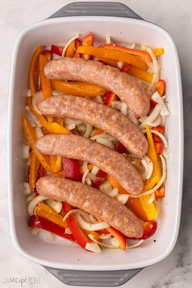 sausages added on top of peppers in baking dish.