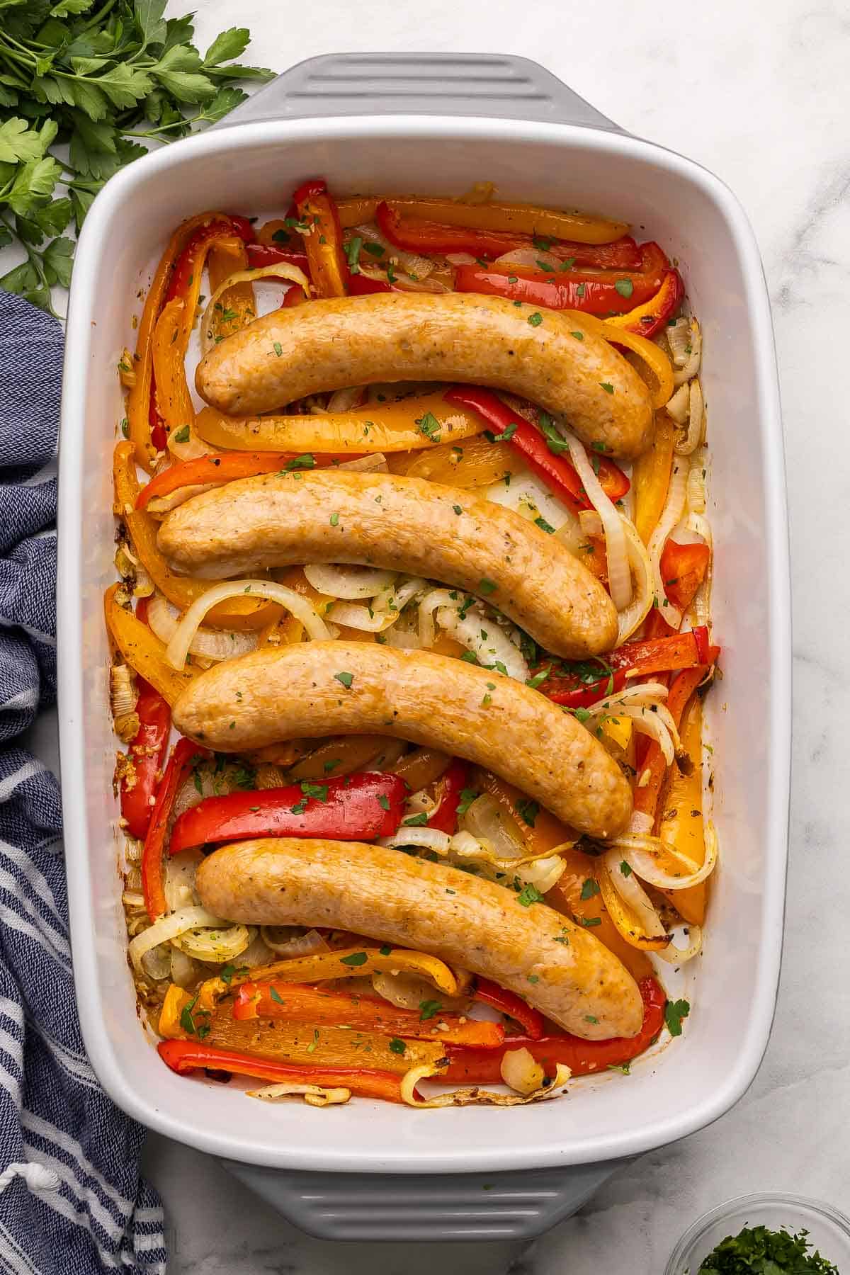 large baking dish filled with four sausages and peppers with parsley beside.