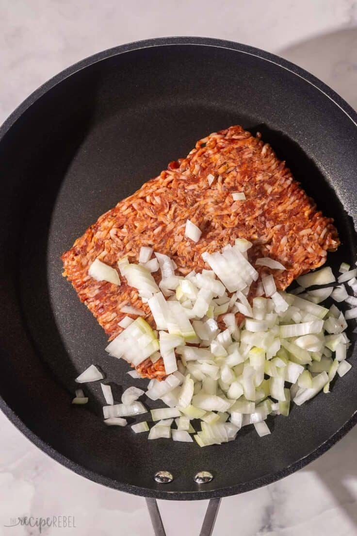 italian sausage with chopped onions in a black pan.