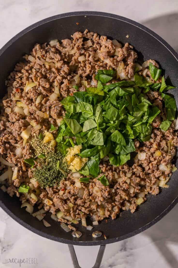 spinach and spices added to other ingredients in pan.