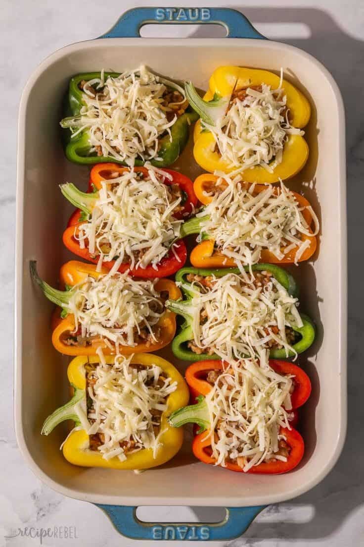 stuffed peppers in baking dish topped with shredded cheese.