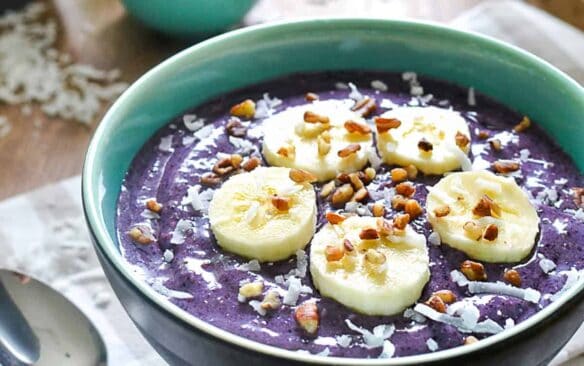 triple berry banana smoothie bowl in a blue bowl with a spoon on the side.