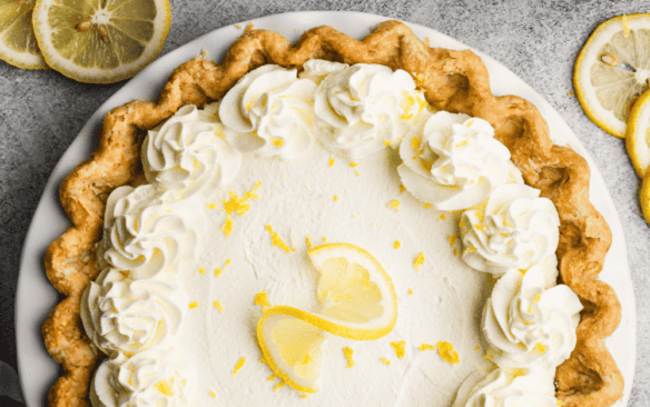 lemon cream pie on a gray background with lemons in a bowl to the side.