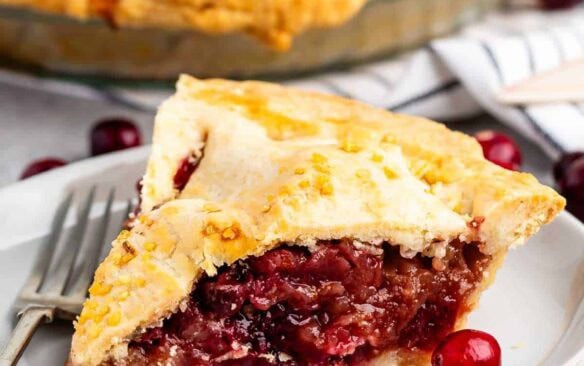 slice of apple cranberry pie on a white plate with a fork.