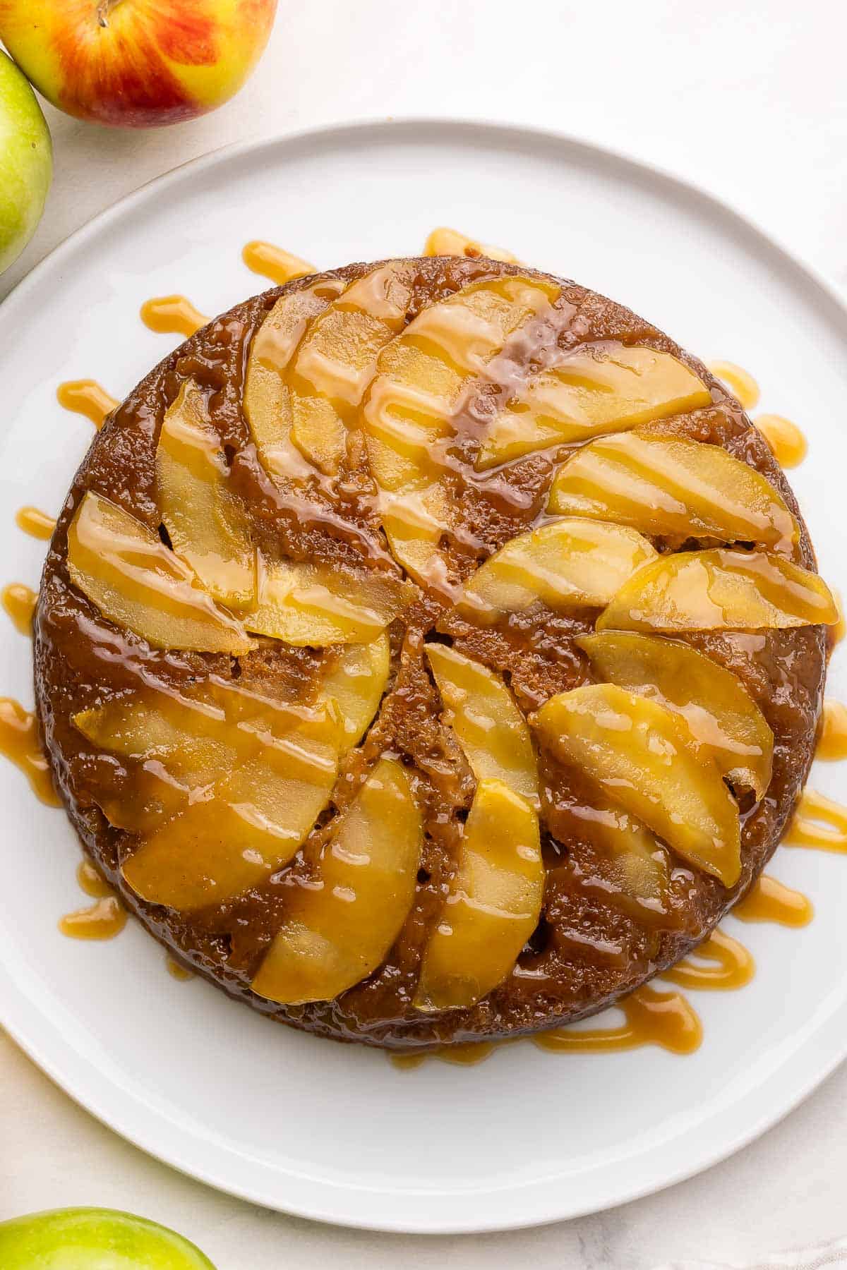 overhead image of apple upside down cake on white plate with caramel sauce.