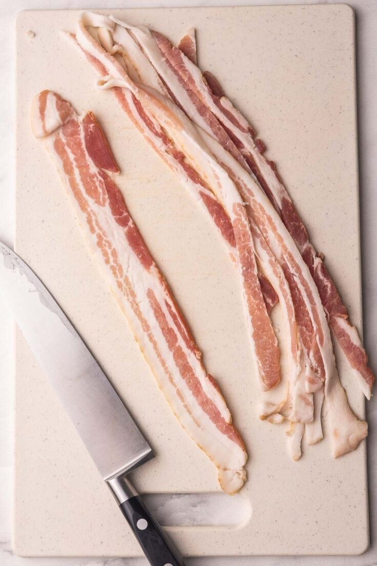 bacon slices on cutting board with a knife beside.