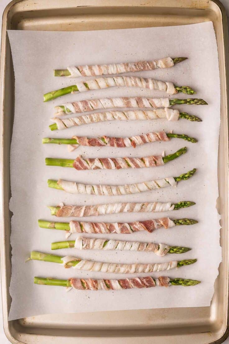 asparagus wrapped in bacon on a parchment lined sheet.