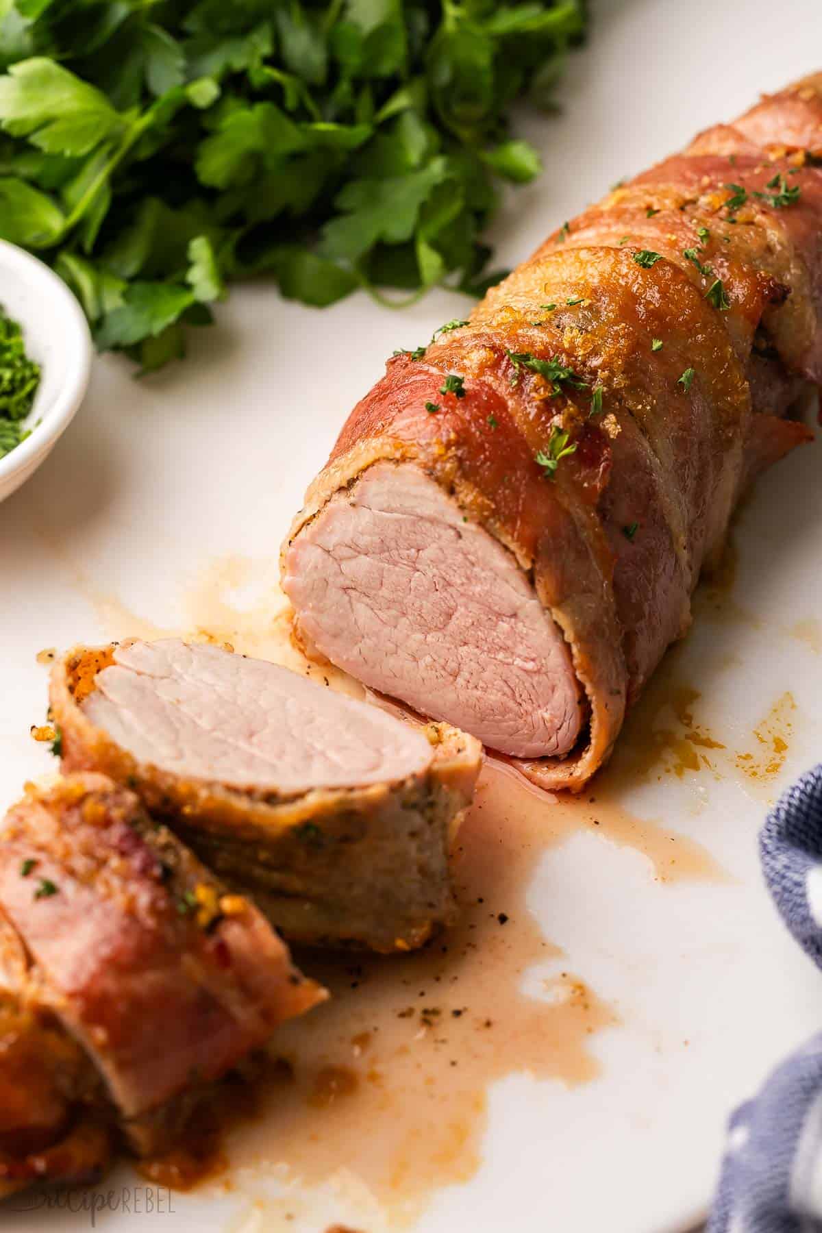 sliced bacon wrapped pork tenderloin on a cutting board.