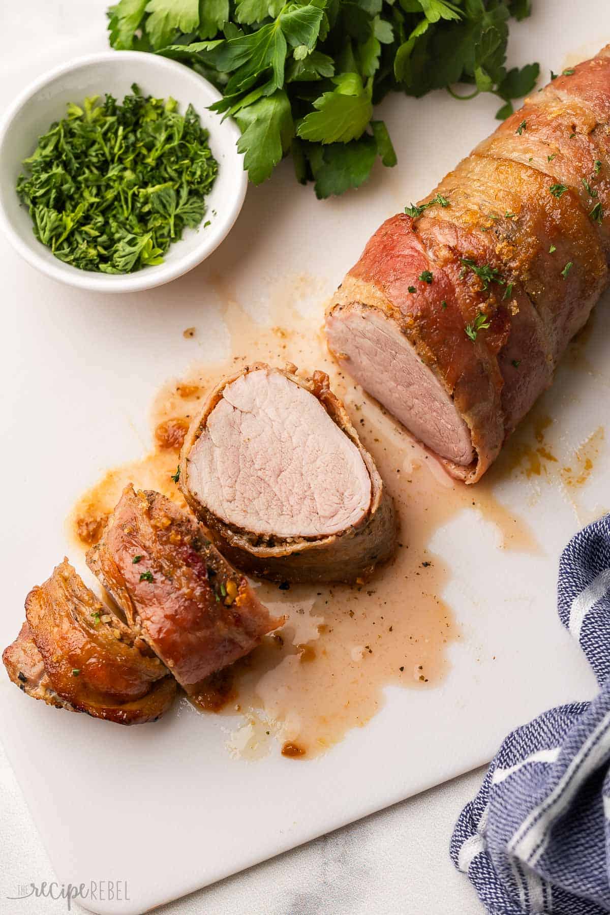 three slices of bacon wrapped pork tenderloin on a cutting board.