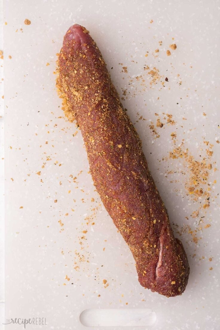 a pork tenderloin on a cutting board covered in a spice rub.