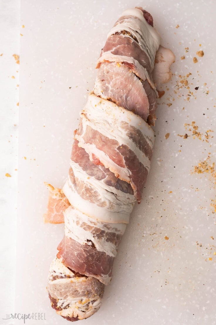 pork tenderloin wrapped in bacon on a cutting board.