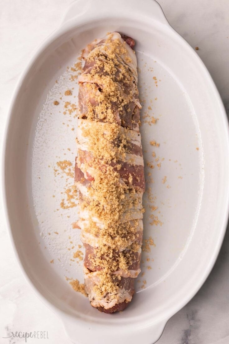 white baking dish with a pork tenderloin in it topped with brown sugar.