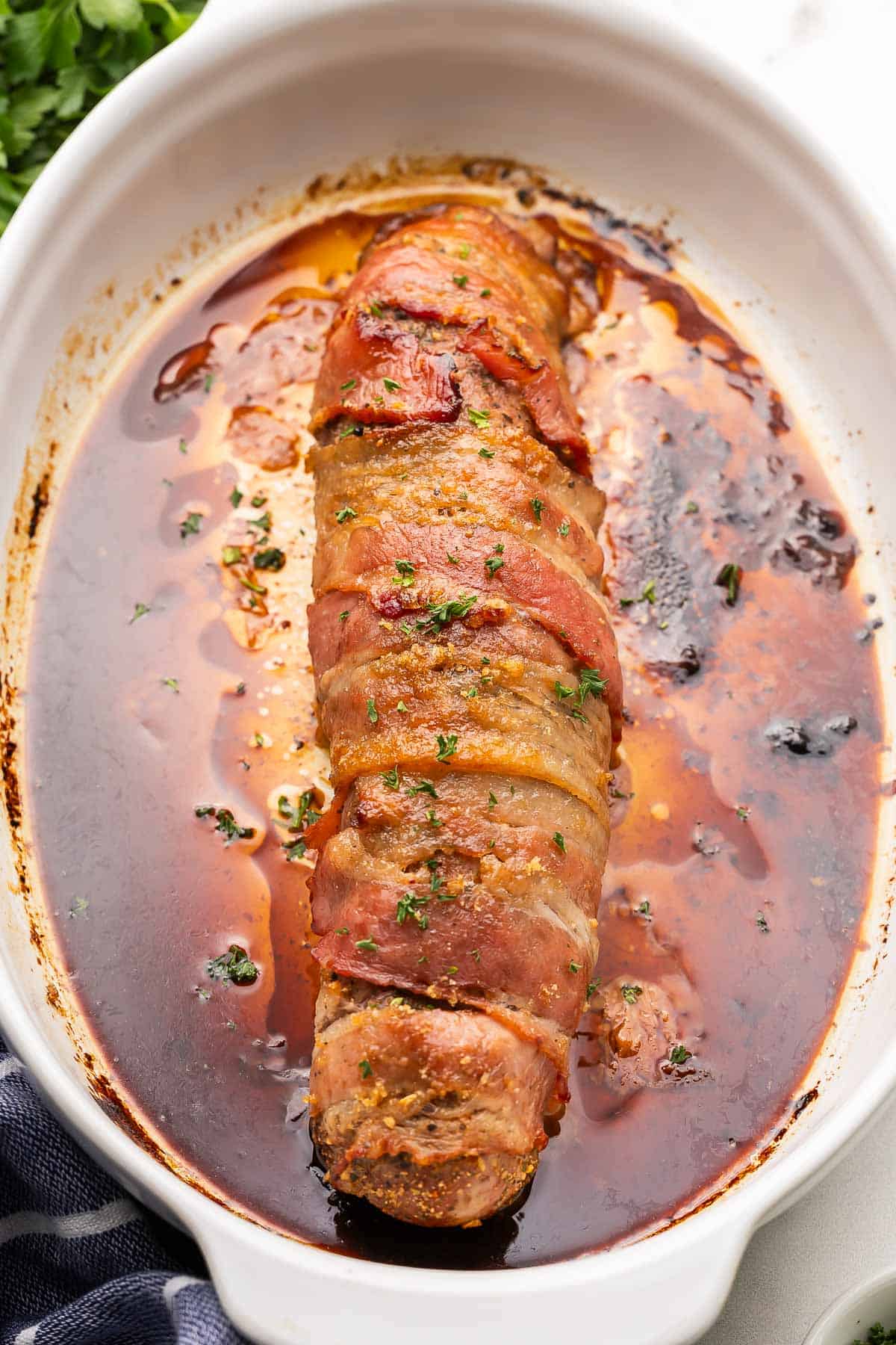 cooked bacon wrapped pork tenderloin in a white dish.