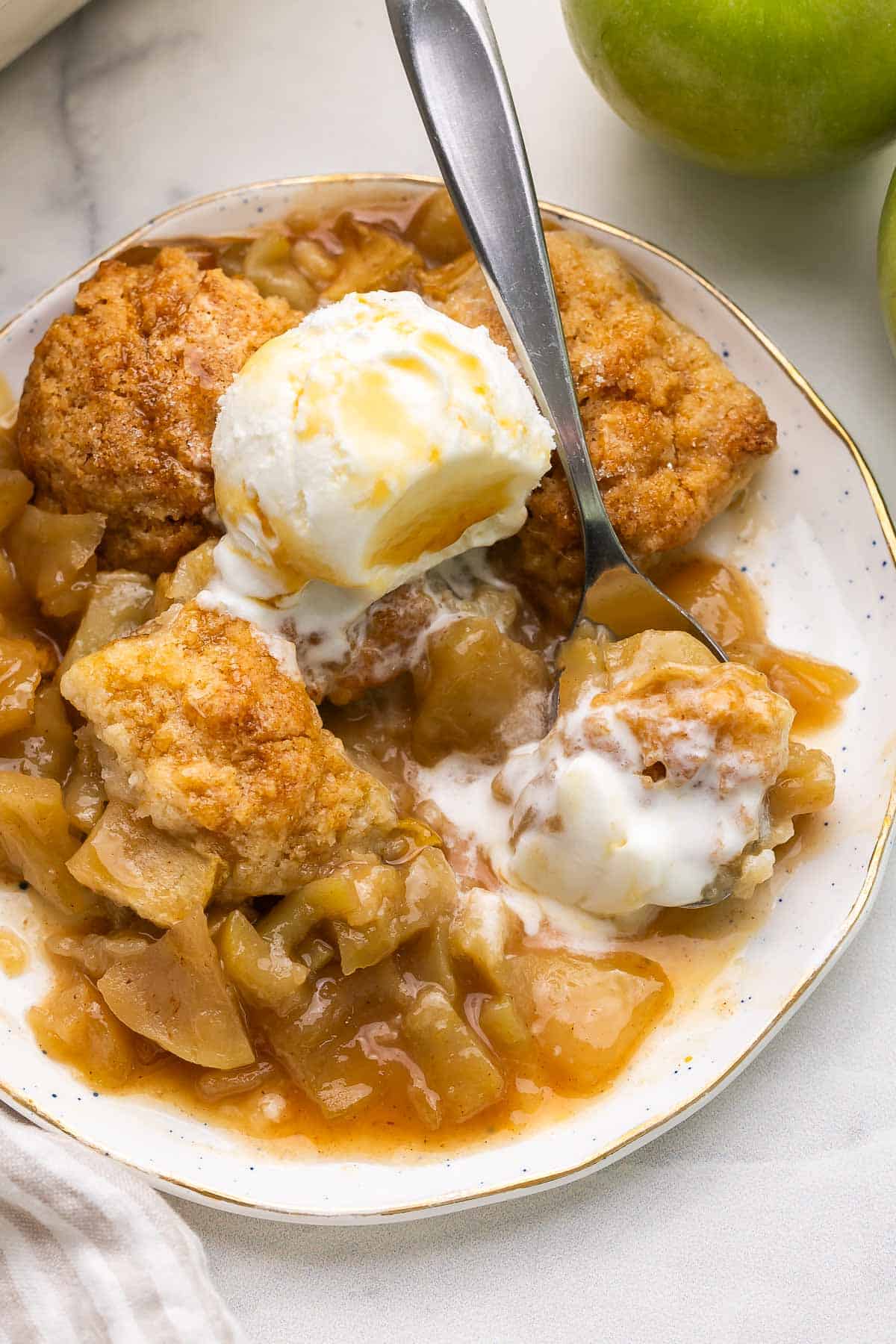 caramel apple cobbler on a white plate with ice cream.