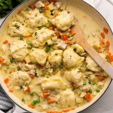 square image of chicken and dumplings in a cream colored braiser.