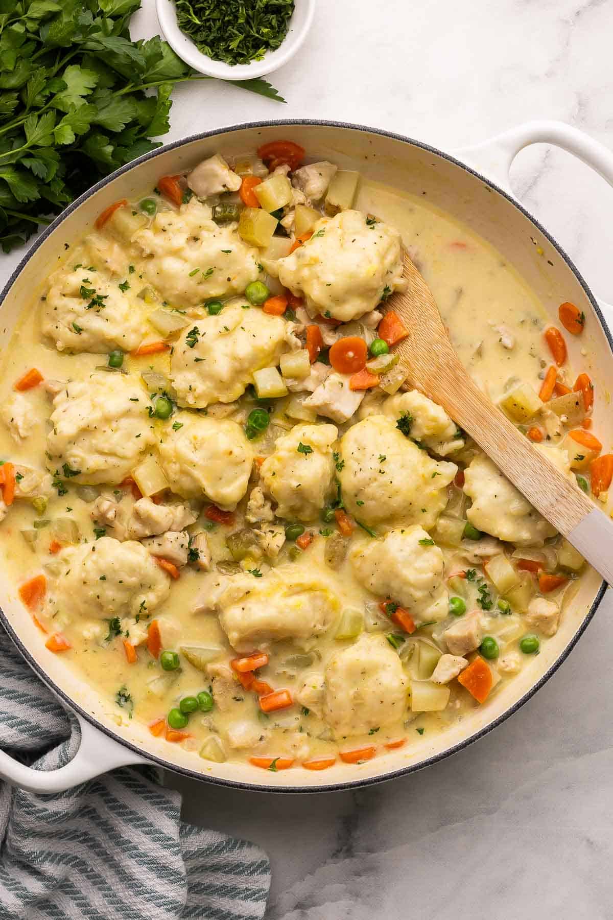 overhead image of chicken and dumplings in a skillet with a wooden spoon.