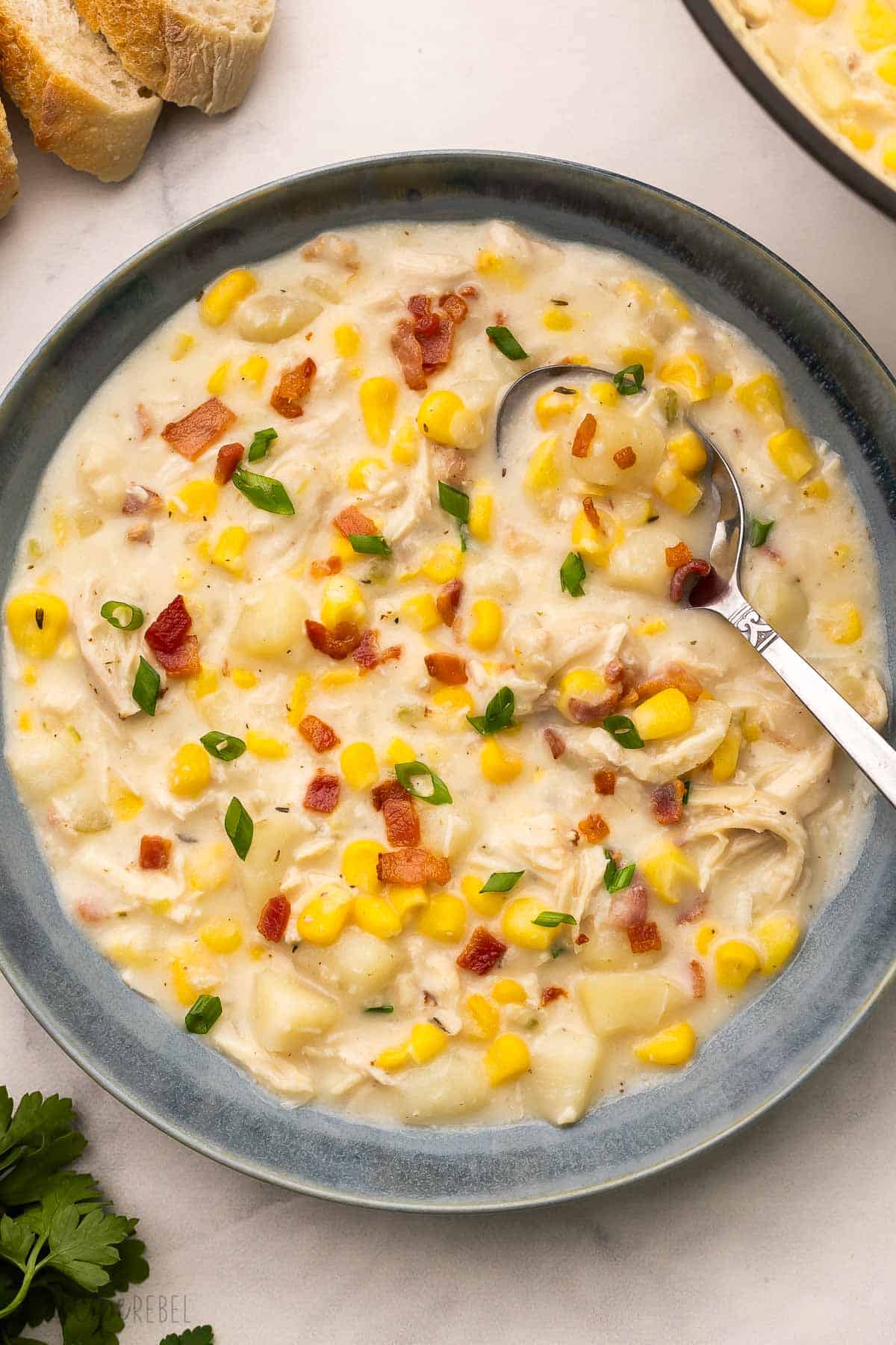 blue bowl filled with chicken corn chowder and a spoon in it.
