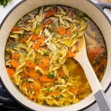 wooden ladle in pot of chicken noodle soup.