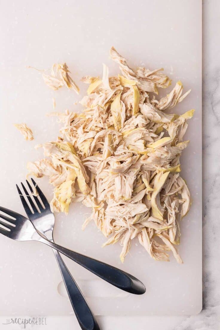 shredded chicken on a cutting board with two forks beside.