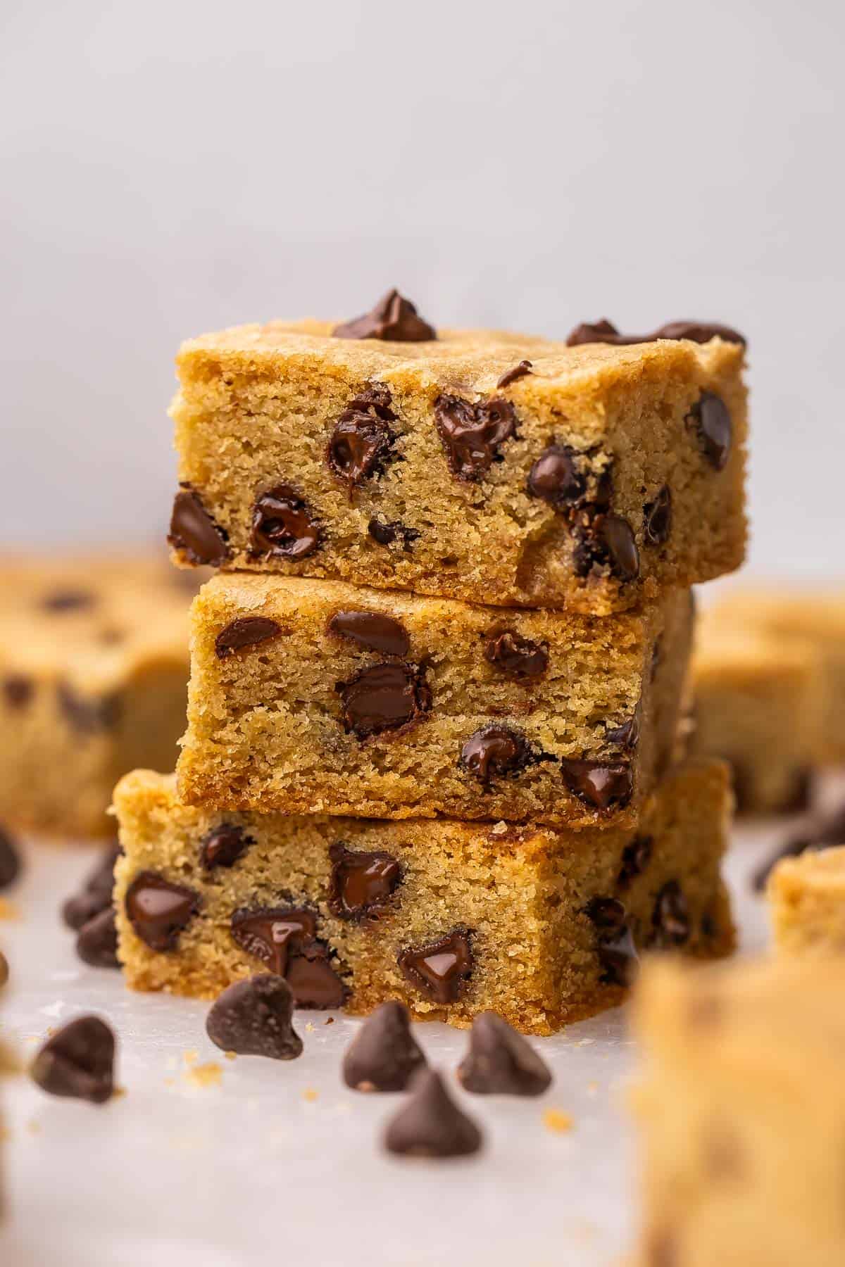 a stack of chocolate chip cookie bars with chocolate chips scattered around.