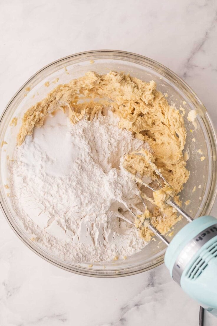flour added to bowl with cookie dough and mixer beside.