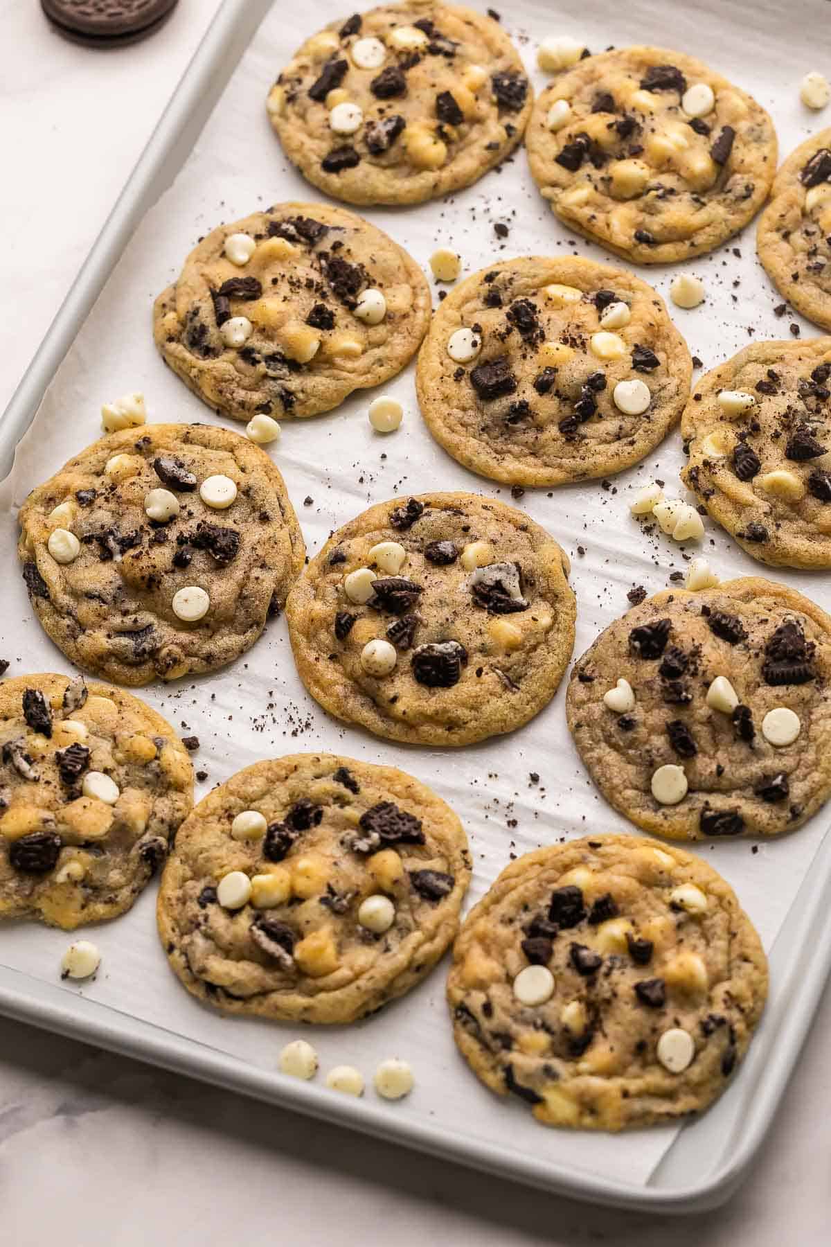 These Cookies and Cream Cookies are everything you love about the classic combo in chewy cookie form! They're made with Oreo cookie chunks, white chocolate chips, and a basic cookie base for a fun twist on the iconic duo. | cookie recipe | oreo cookies | oreo desserts | baking from scratch | homemade cookies  sheet pan full of cookies and cream cookies with chocolate chips beside.