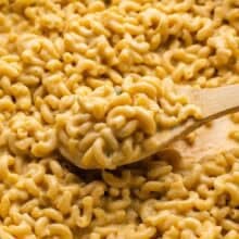 wooden spoon scooping skillet macaroni and cheese from pan.