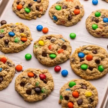 monster cookies on parchment paper with M&M's lying between them.