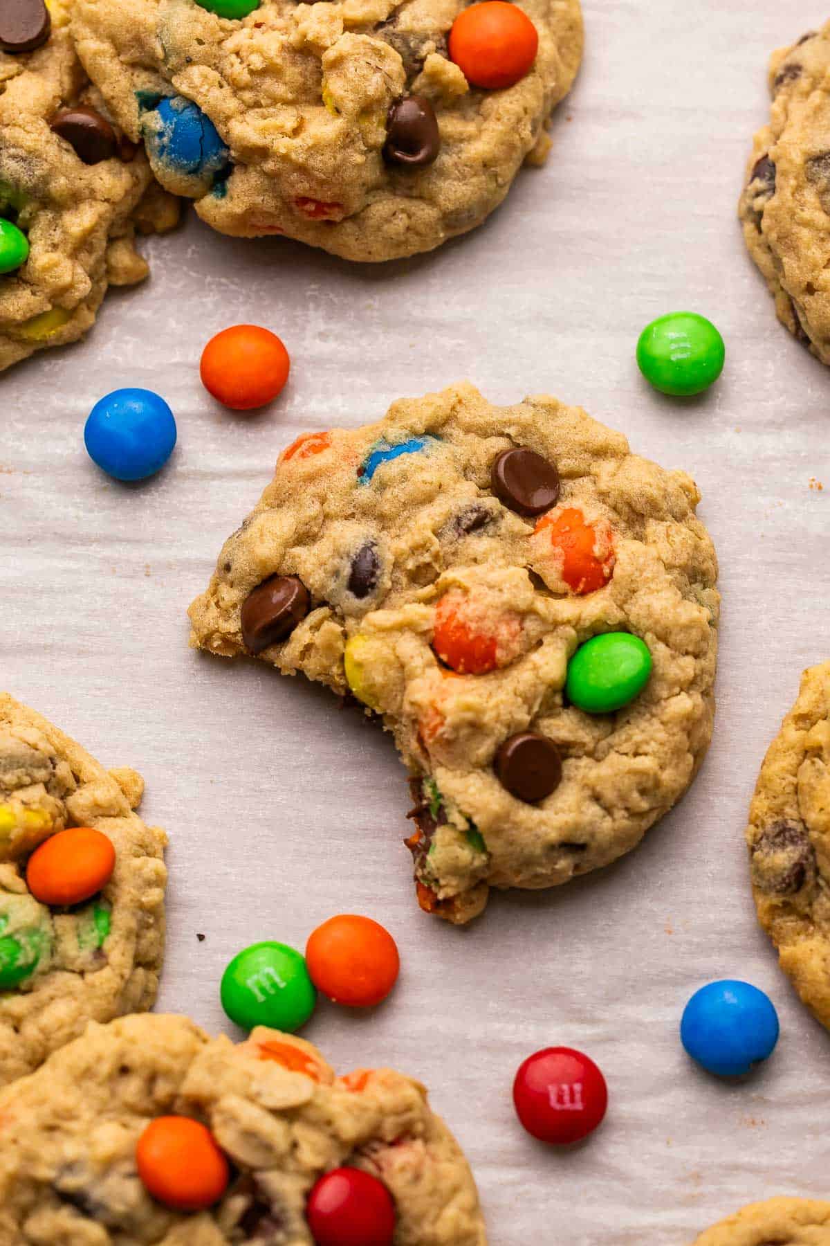 Classic Monster Cookies are loaded with creamy peanut butter, chewy old-fashioned oats, melty chocolate chips, and colorful M&Ms. They're the perfect cookie for those who like a little bit of everything! #cookie #recipe | cookie recipe | cookies recipe | peanut butter cookies | oatmeal cookies | m&m cookies | dessert recipe | baking recipe a monster cookie with a bite missing and M&M's scattered beside with other cookies.