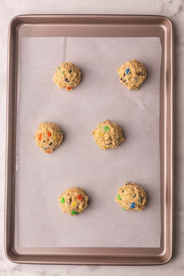 six unbaked dough balls on a parchment lined sheet.