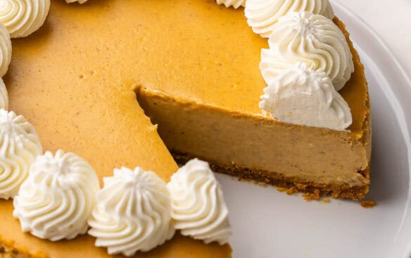 pumpkin cheesecake topped with whipped cream on a white plate.