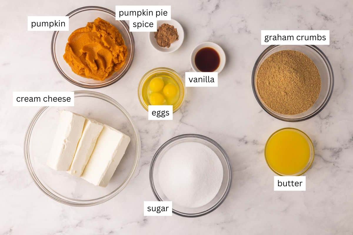 This baked Pumpkin Cheesecake has a super creamy filling and is packed with warm spices and cozy pumpkin flavor! It's easier than the rest, thanks to one secret method. No water bath and no cracks! #pumpkin #cheesecake #dessert | dessert recipes | pumpkin recipes | pumpkin dessert | baked cheesecake recipe | fall dessert | thanksgiving dessert ingredients needed for pumpkin cheesecake in bowls.