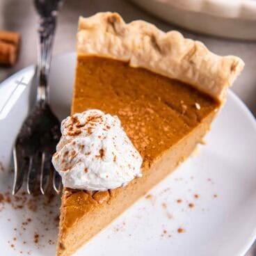 slice of pumpkin pie on a white plate with whipped cream.