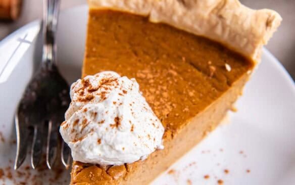 slice of pumpkin pie on a white plate with whipped cream.