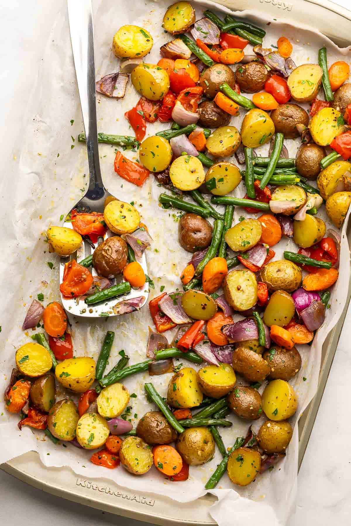 overhead image of roasted vegetables on a baking sheet with parchment paper.