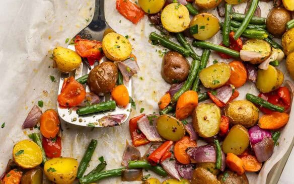 square image of roasted vegetables on a baking sheet with a metal spatula.