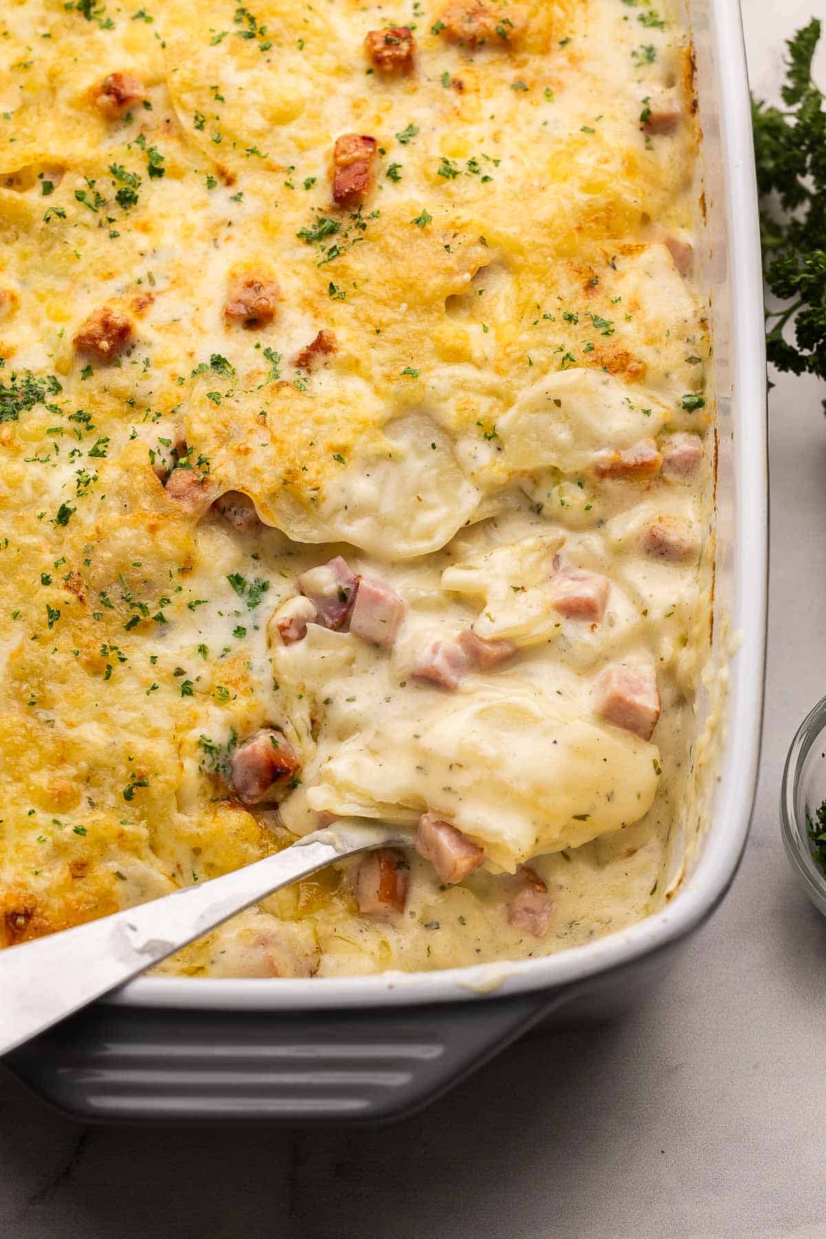 large spoon scooping scalloped potatoes out of pan.