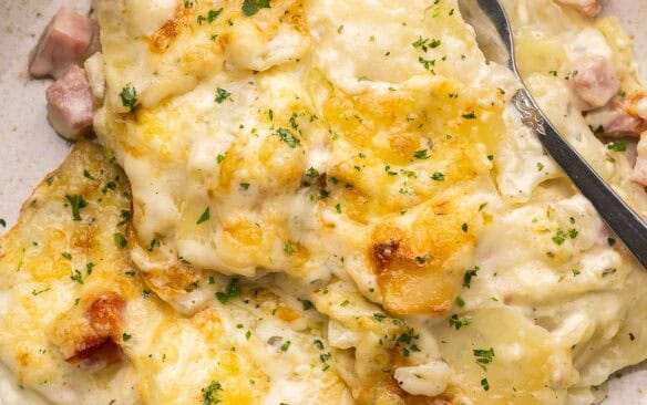 scalloped potatoes and ham on a plate with a fork in it.